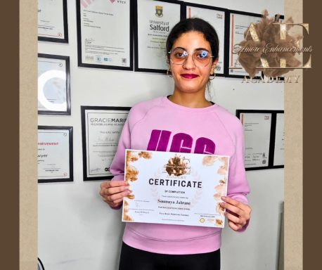 A smiling woman holds a certificate in front of a wall of framed certificates.